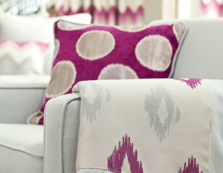 Pinkfarbenes Kissen und passende Decke auf einem grauen Sessel
