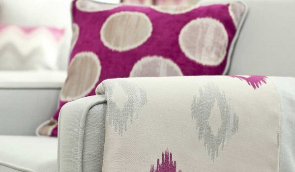 Pinkfarbenes Kissen und passende Decke auf einem grauen Sessel