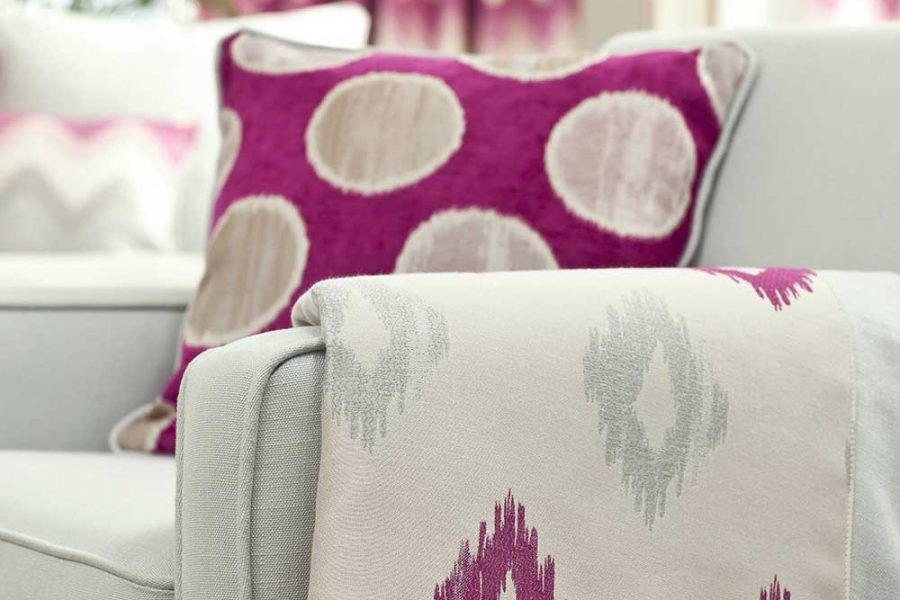 Pinkfarbenes Kissen und passende Decke auf einem grauen Sessel